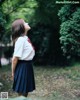 A woman in a school uniform standing in the woods.