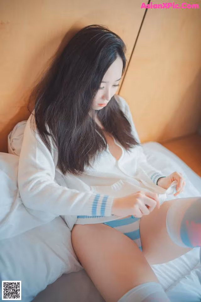 A woman sitting on top of a bed holding a cell phone.