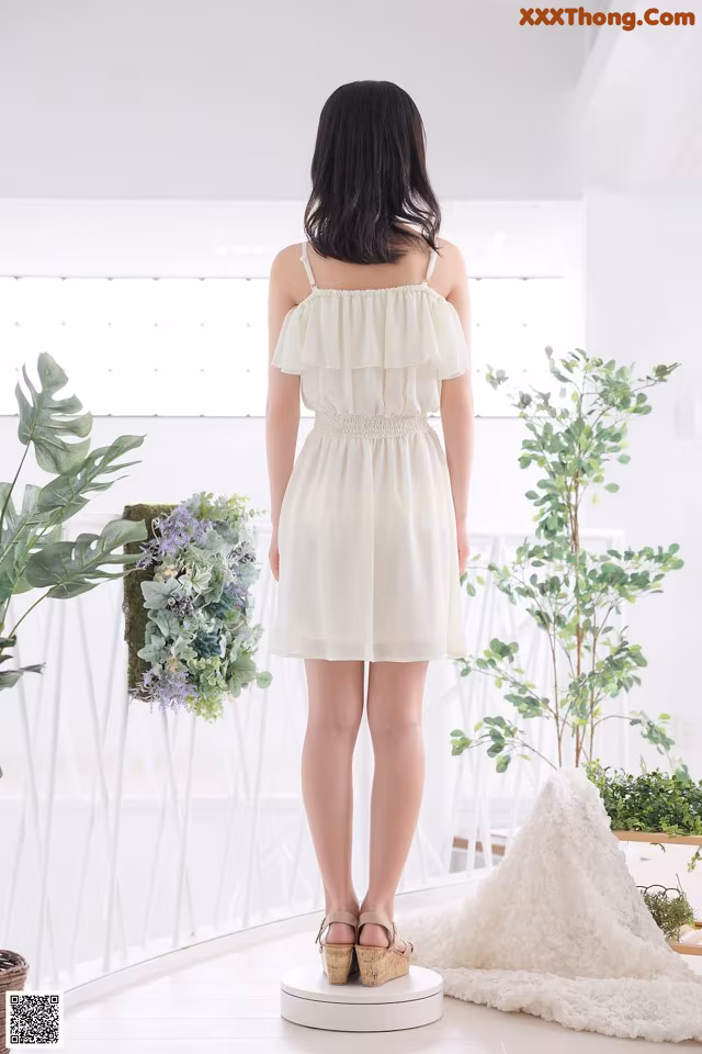A woman in a white dress standing in front of a window.