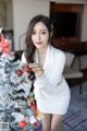 A woman in a white dress standing next to a Christmas tree.