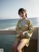 A woman in a kimono sitting on a ledge by the ocean.