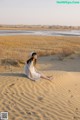 A woman sitting on top of a sand dune in the desert.