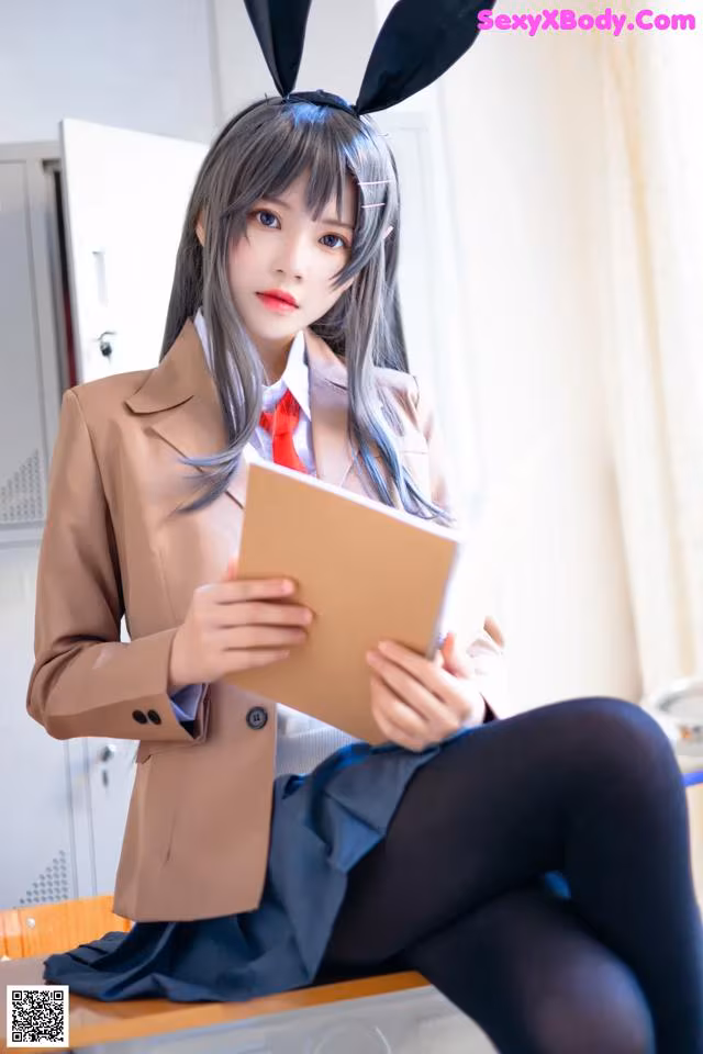 A woman in a bunny suit sitting on a desk holding a book.