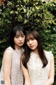 Two young women standing next to each other in front of a tree.