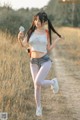 A woman in shorts and a white tank top is running in a field.