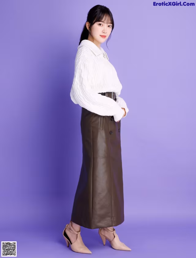 A woman wearing a white sweater and a brown leather skirt.