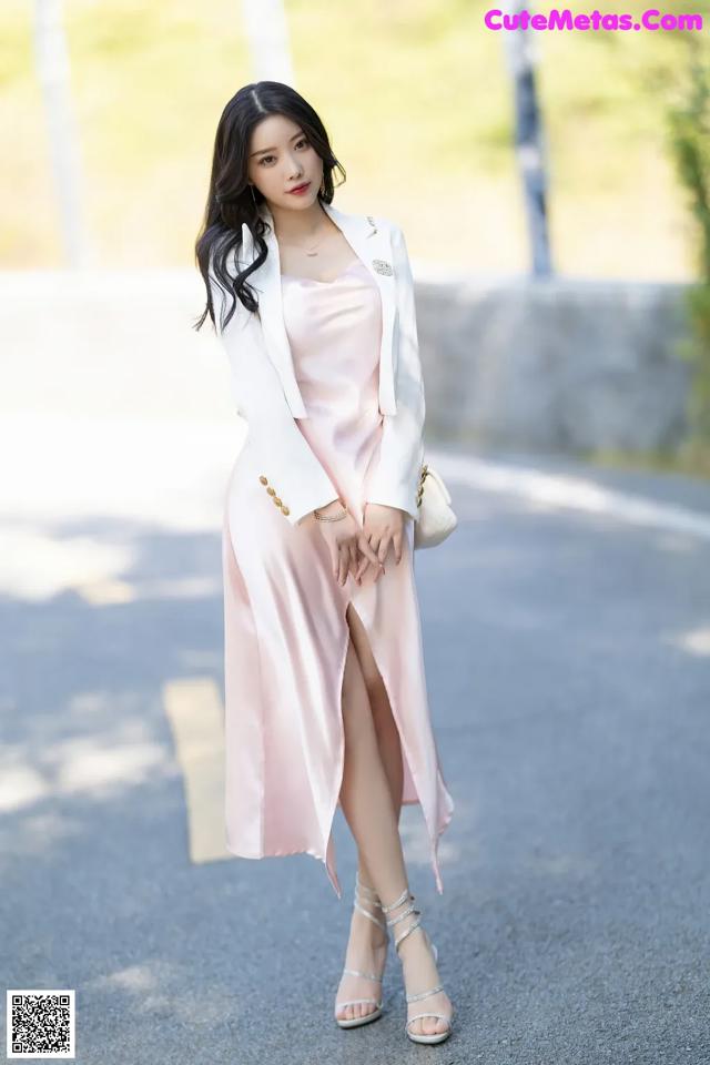 A woman in a pink dress and white blazer posing for a picture.