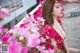 A woman in a red dress sitting on a bench surrounded by pink flowers.