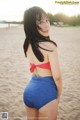 A woman in a red and white polka dot bikini top and blue shorts on the beach.