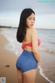 A woman in a red and white polka dot bikini top and blue shorts on the beach.