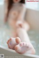 A naked woman sitting in a bathtub with her feet in the water.