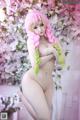 A naked woman with pink hair is posing in front of a flowering tree.